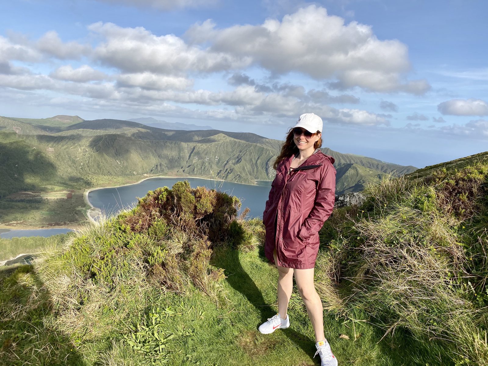 Someone standing on a grassy ridge above a blue crater lake in the Azores
