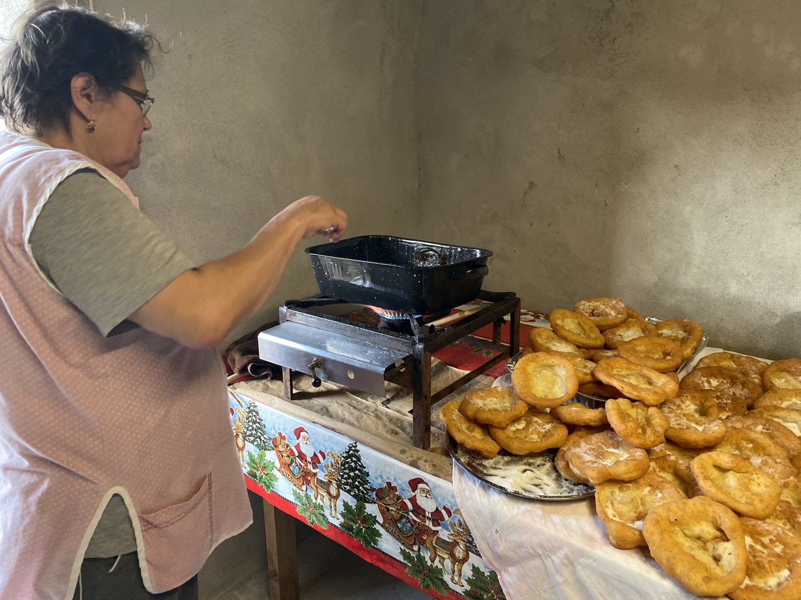 A woman frying traditional pastries at a table covered with trays of them