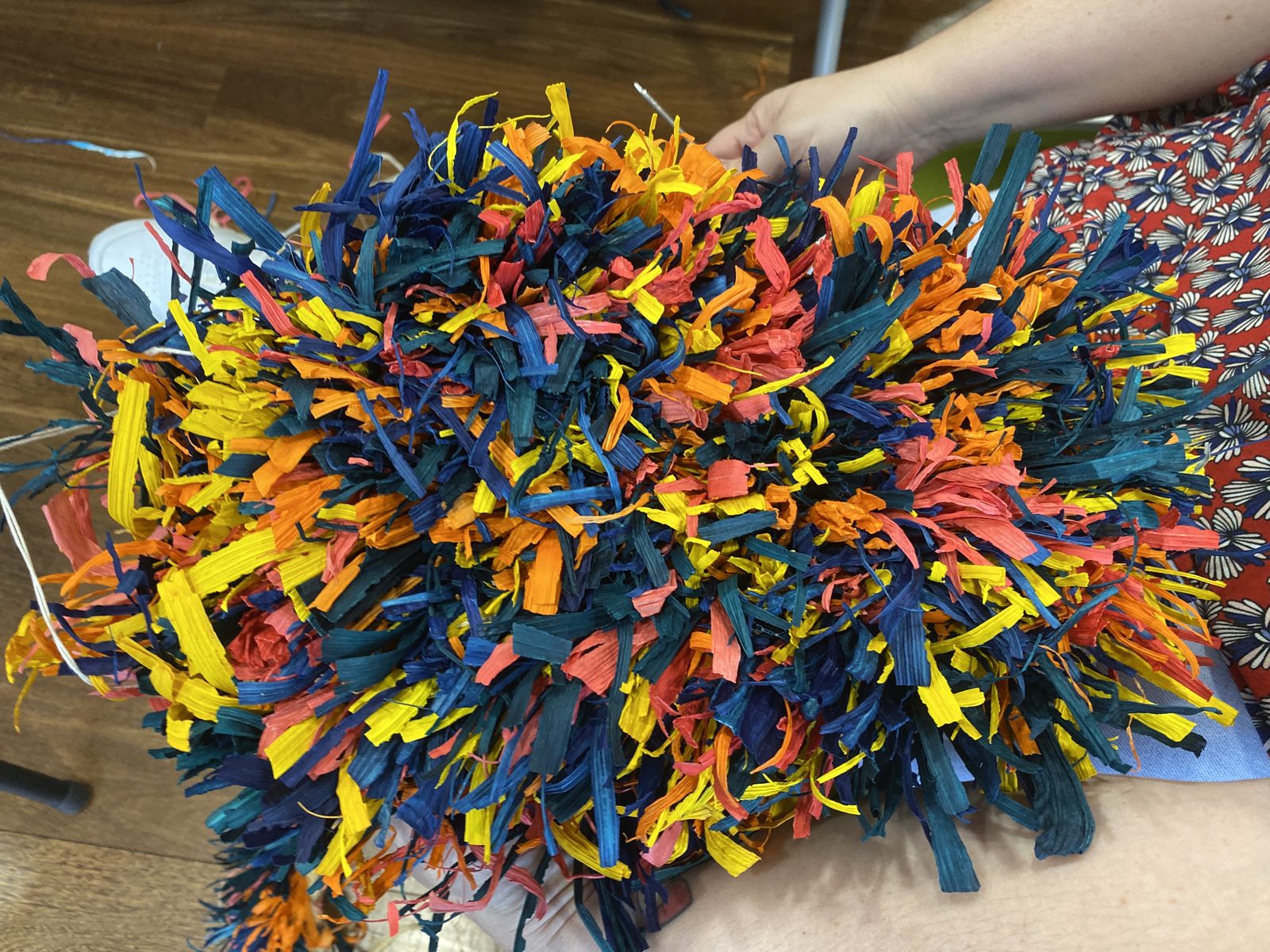 Hands working on a brightly coloured mat woven from strips of dyed material