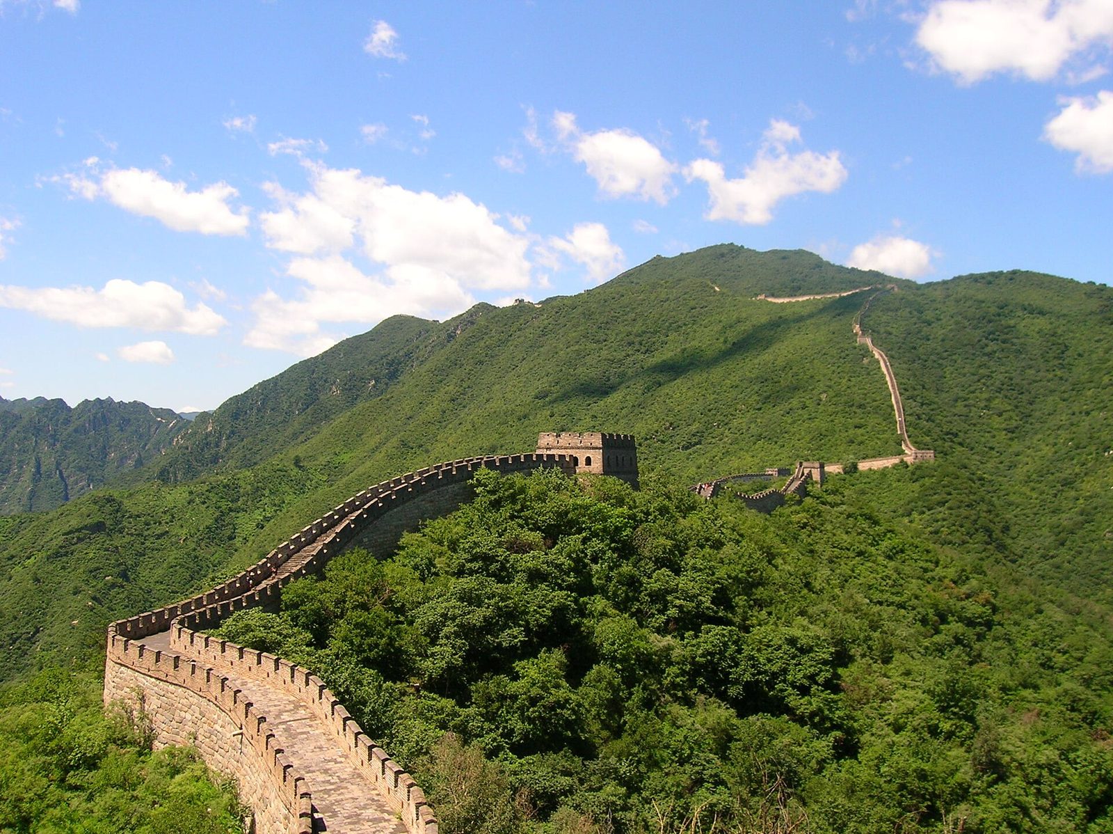A section of the Great Wall of China running along a wooded ridge, watchtowers spaced along it