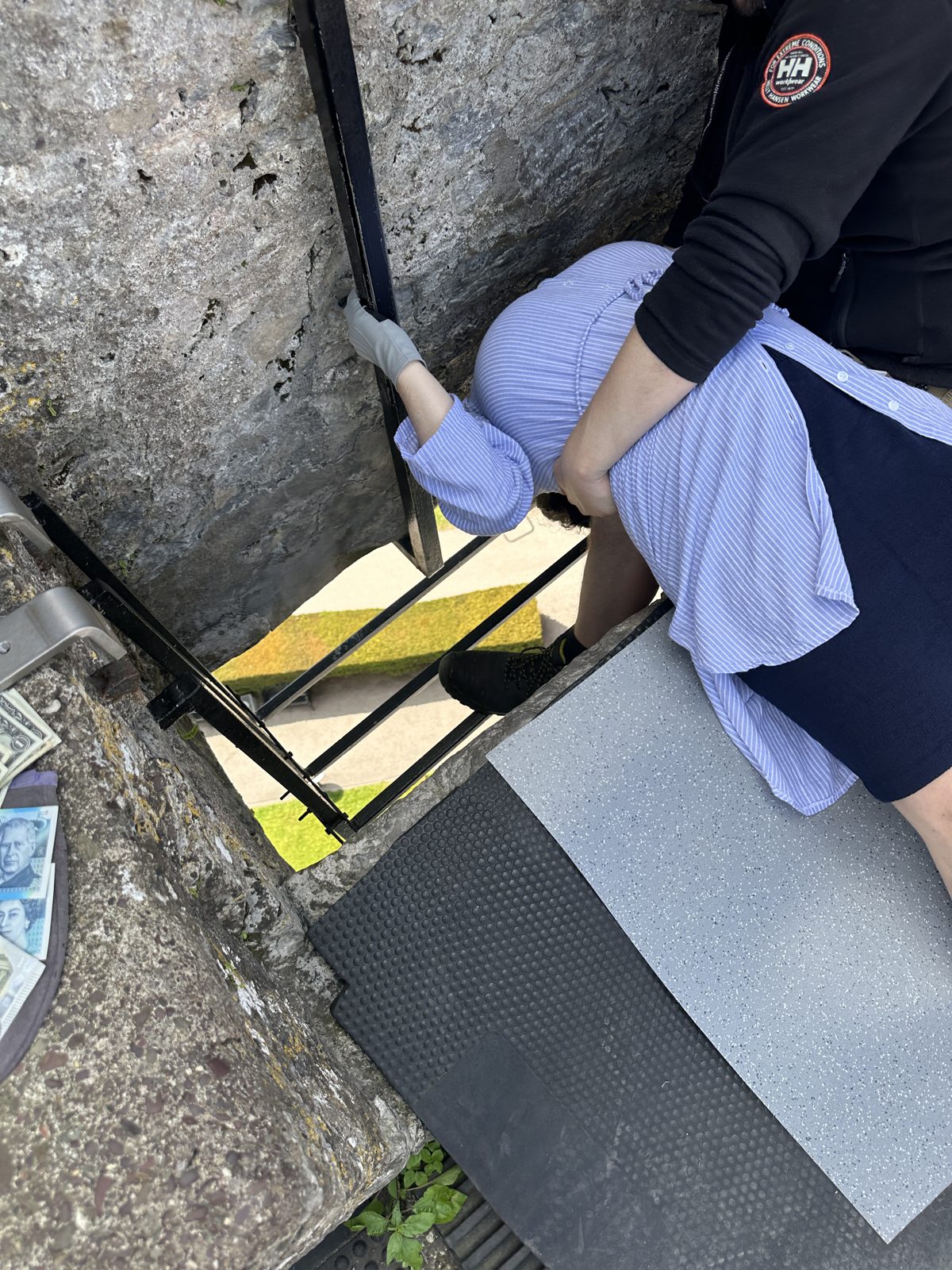 Looking down as someone lies back to kiss the Blarney Stone, held by an attendant, with iron rails and a grating below