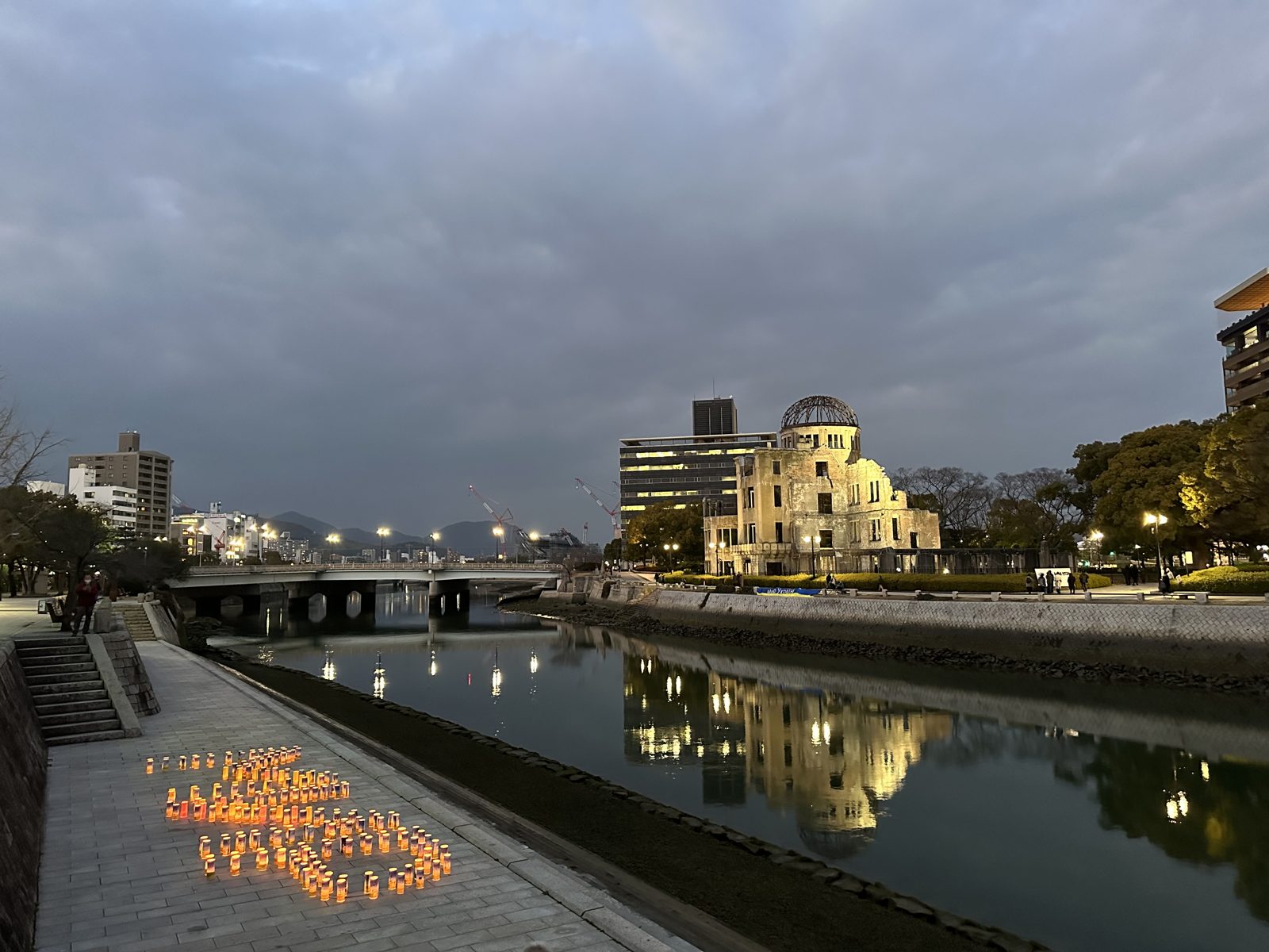 The A-Bomb Dome lit at dusk across the river in Hiroshima, with small lanterns glowing on the bank