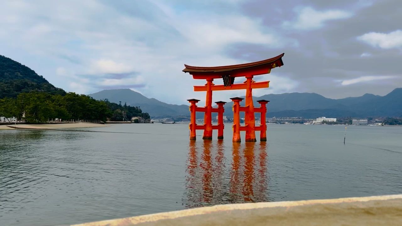 The great red torii gate of Itsukushima standing in the water at high tide, hills behind it across the bay