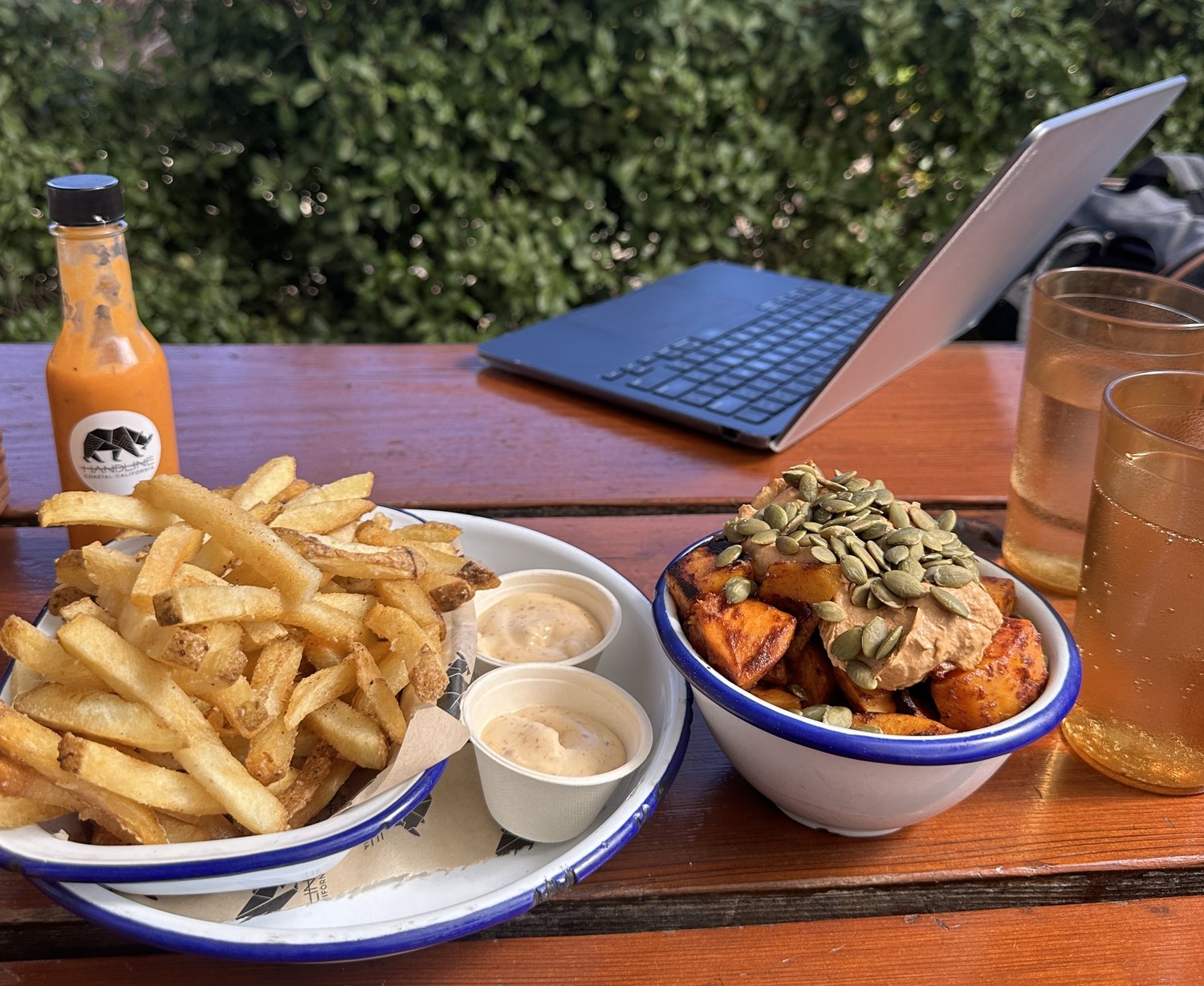 A bowl of fries and a bowl of roasted sweet potato topped with pumpkin seeds and chipotle cream, on a picnic table at Handline in Sebastopol