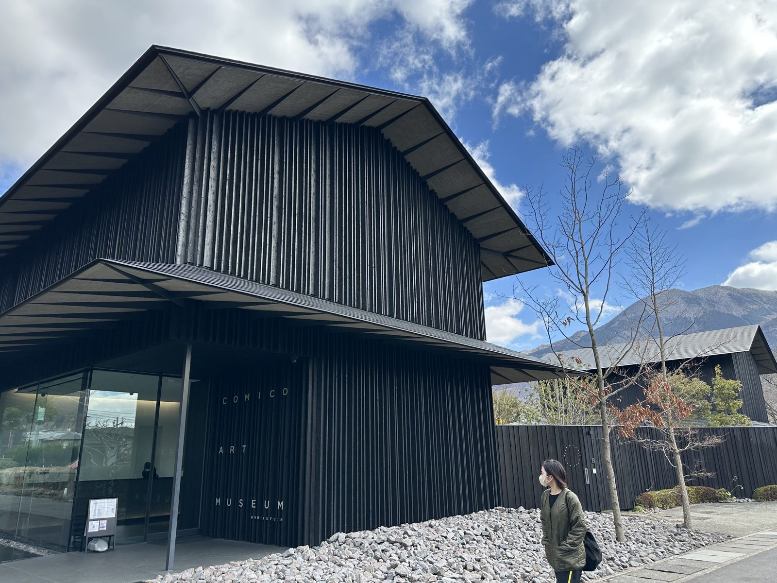 The Comico Art Museum in Yufuin, a black charred timber building with deep eaves, mountains rising behind it