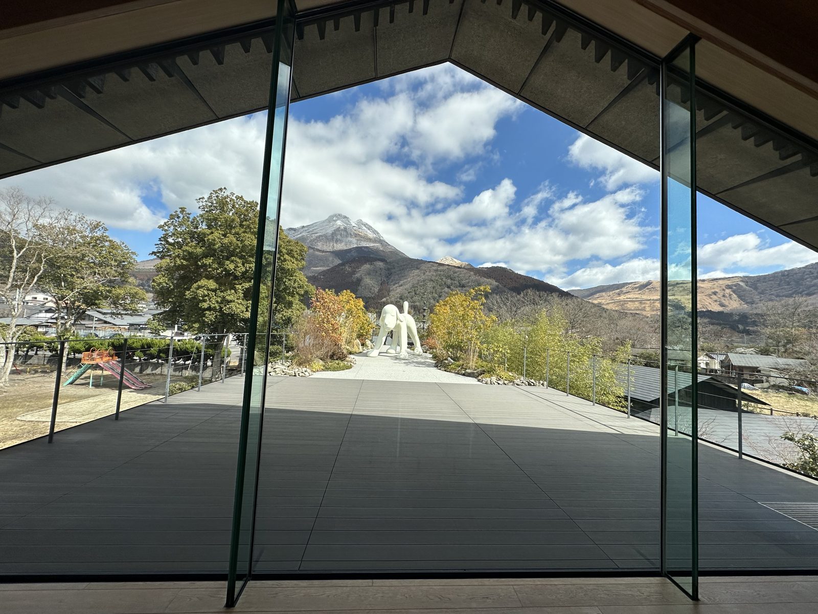 The view from inside the museum, looking out through full height glass to the terrace, the white dog, and the mountains beyond