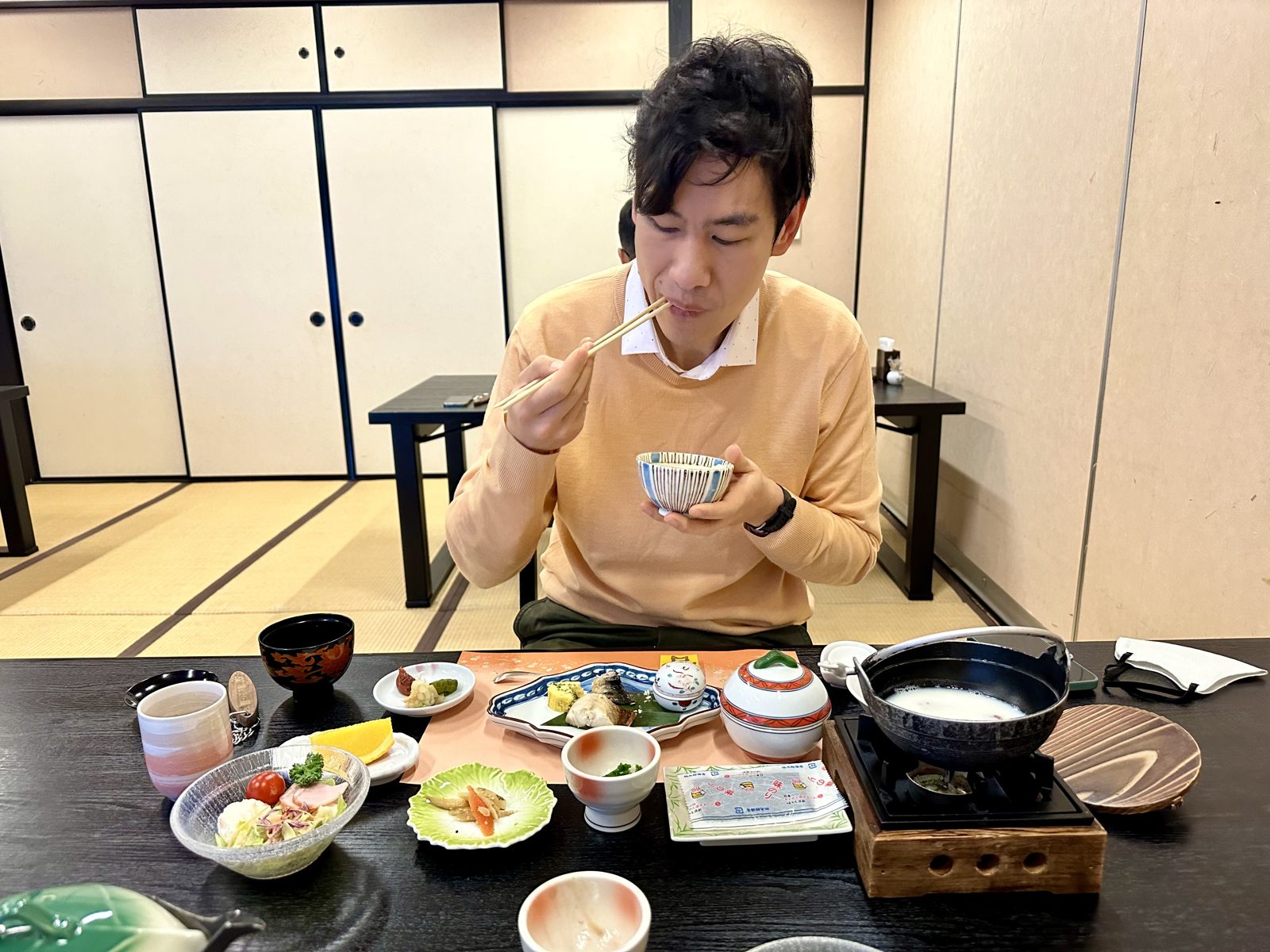 A kaiseki meal laid out on a low table in a tatami room at a ryokan in Yufuin, many small dishes with a lidded pot on a burner