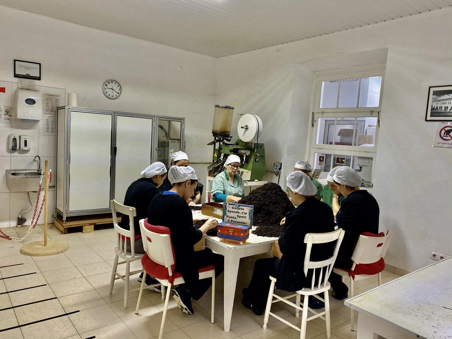 Workers in white hairnets sorting loose black tea by hand around a table in the packing room