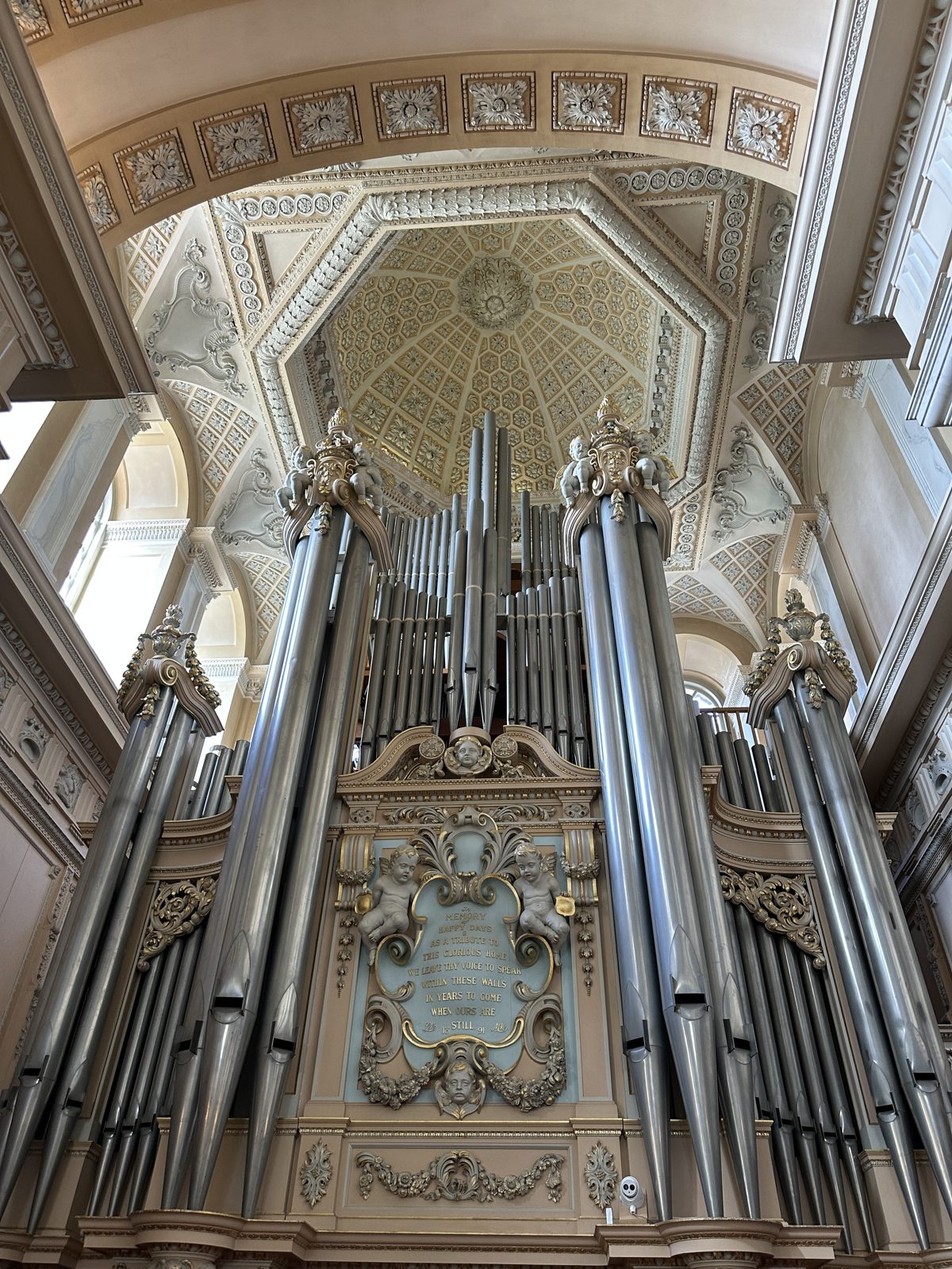 The organ at the end of the Long Library, a bank of tall silver pipes under gilded carving and a painted inscription panel held by cherubs