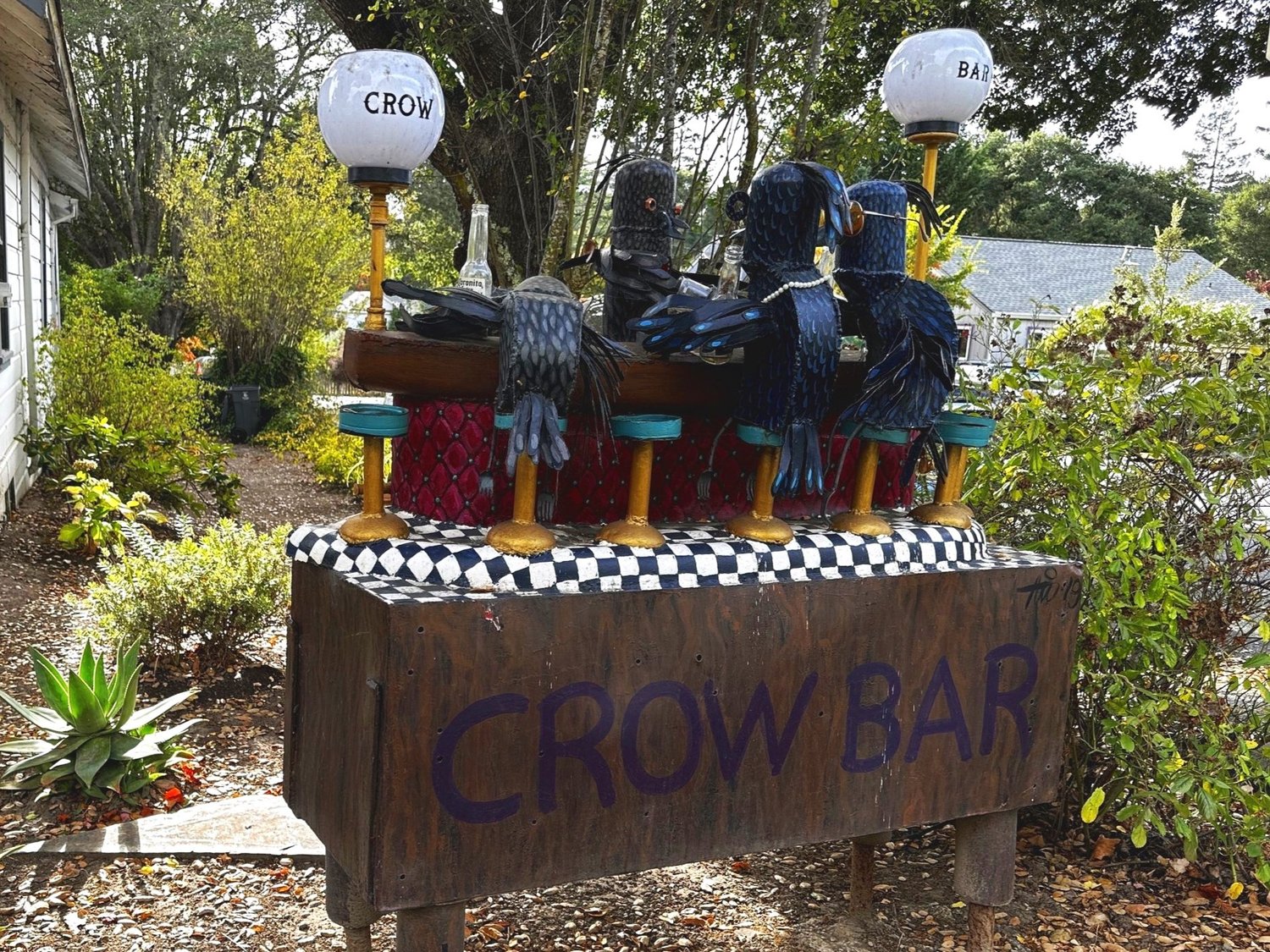 The Crow Bar sculpture, a row of metal crows perched on barstools at a small painted bar