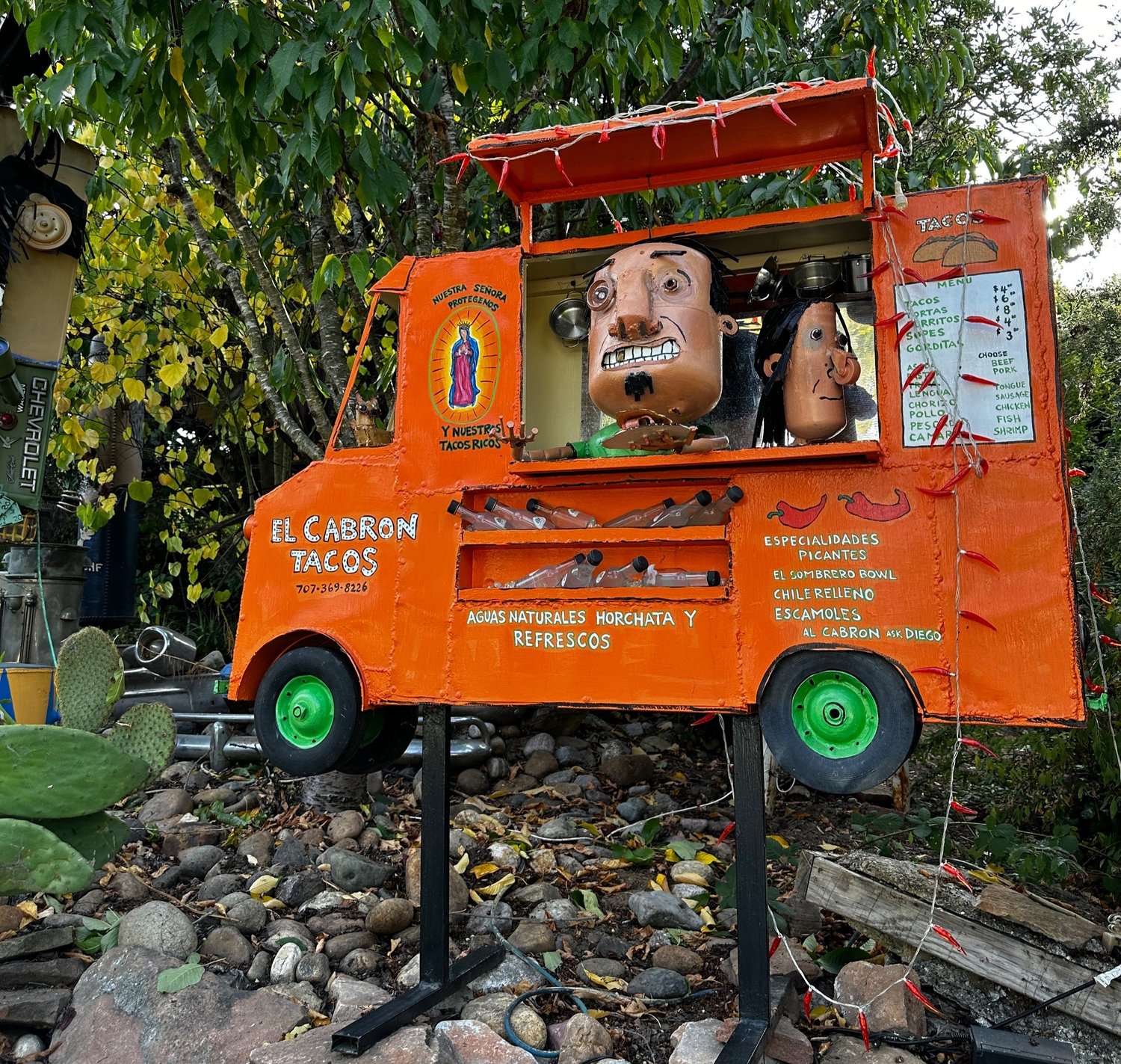 An orange scrap metal taco truck sculpture called El Cabron Tacos, with two figures serving from the window