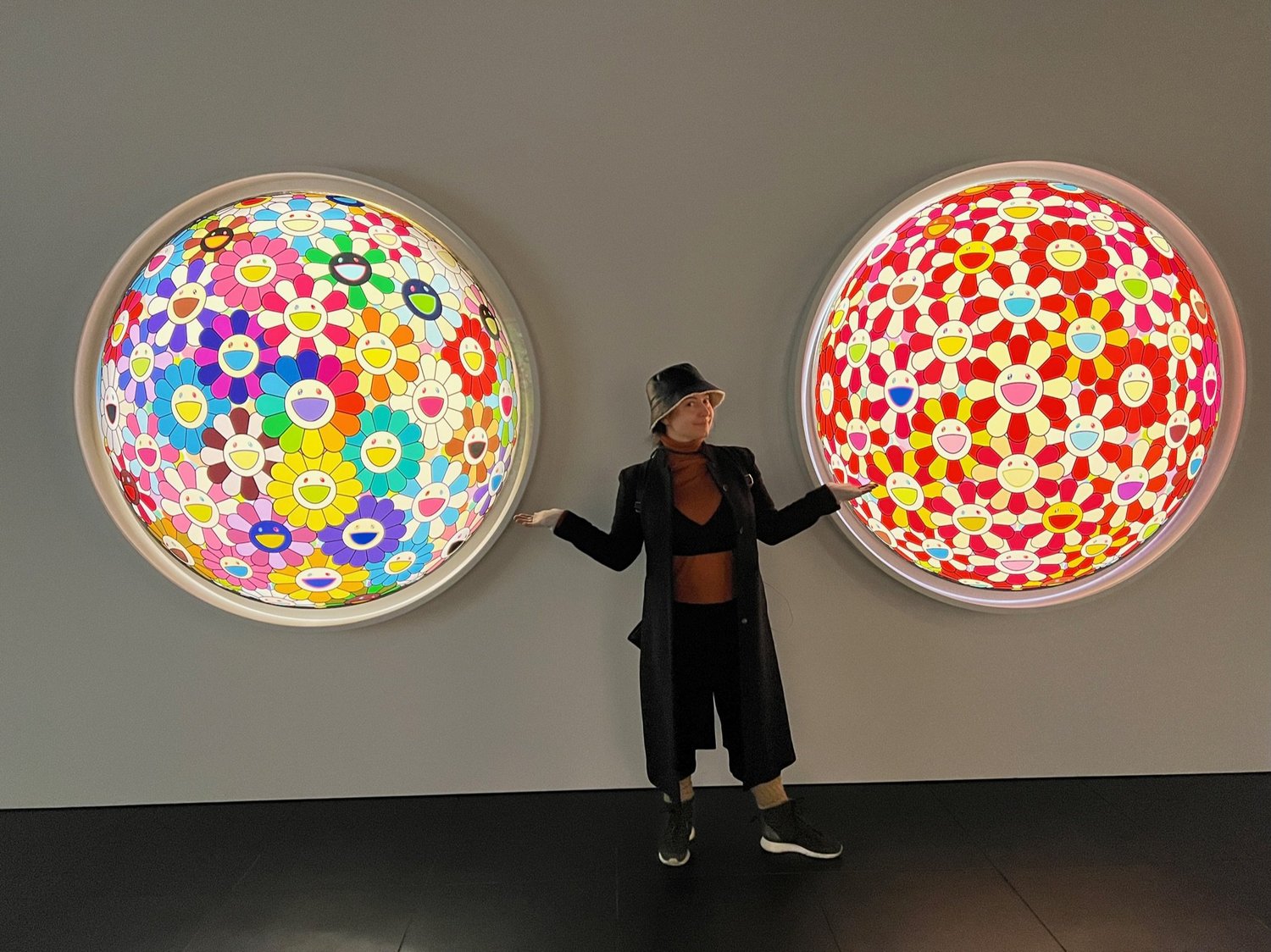 A visitor standing between two round Takashi Murakami panels covered in his smiling flower motif