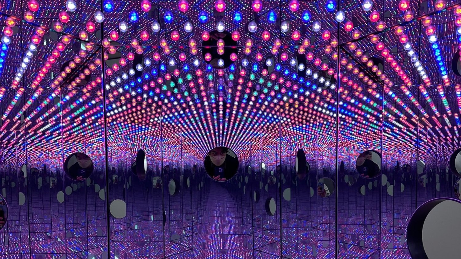 Inside a Yayoi Kusama infinity mirror room, hundreds of coloured lights repeating away in every direction