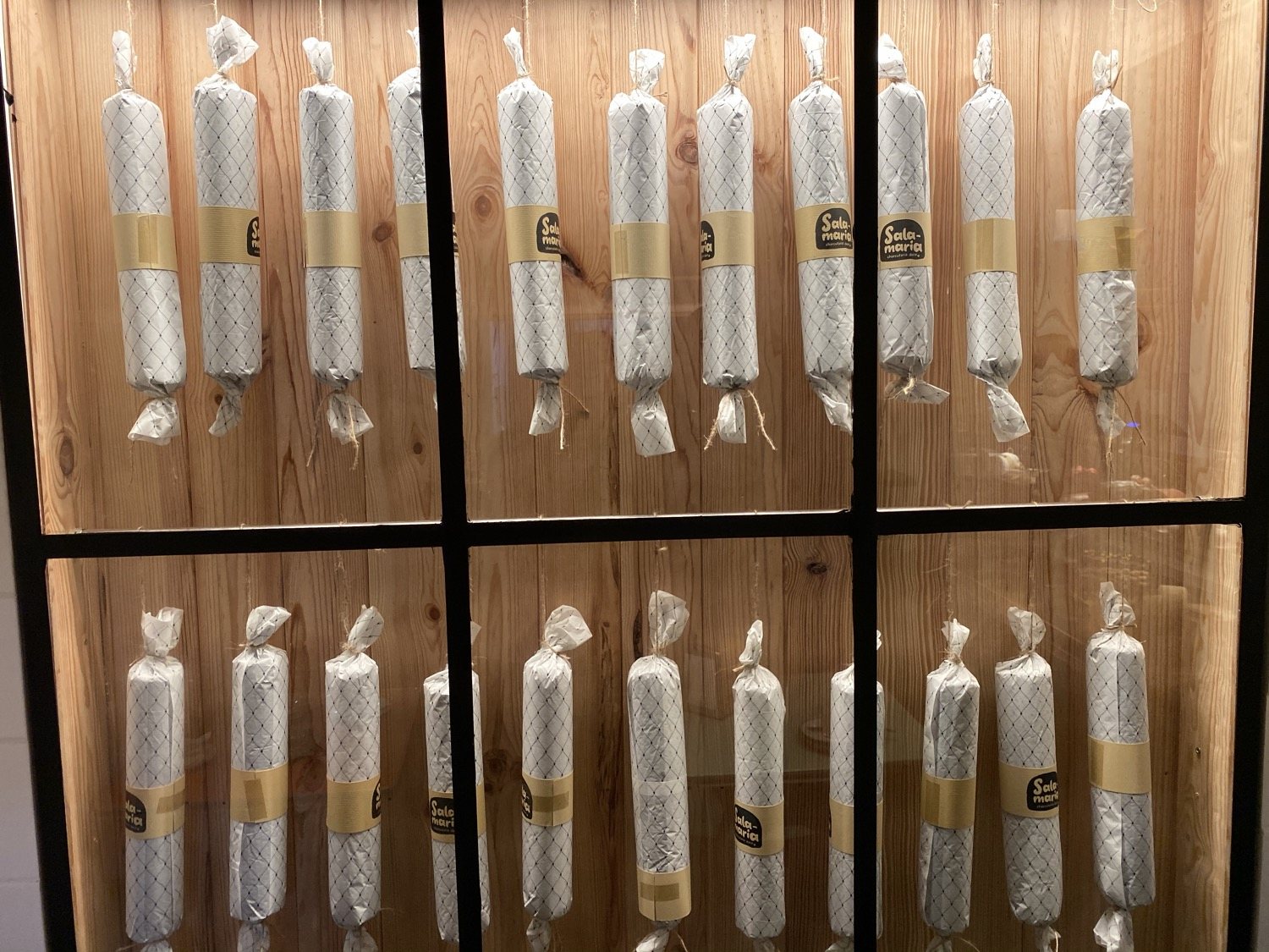 Wrapped rolls of chocolate salami hanging in rows inside a lit wooden display case