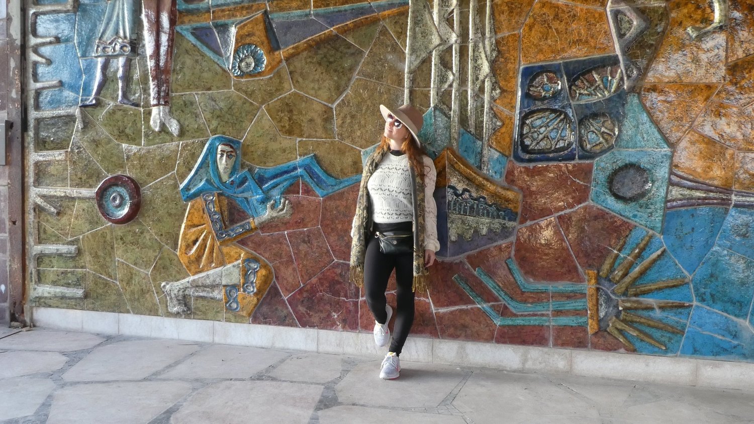 A visitor standing against a large ceramic tile mural in blue, orange and rust coloured panels