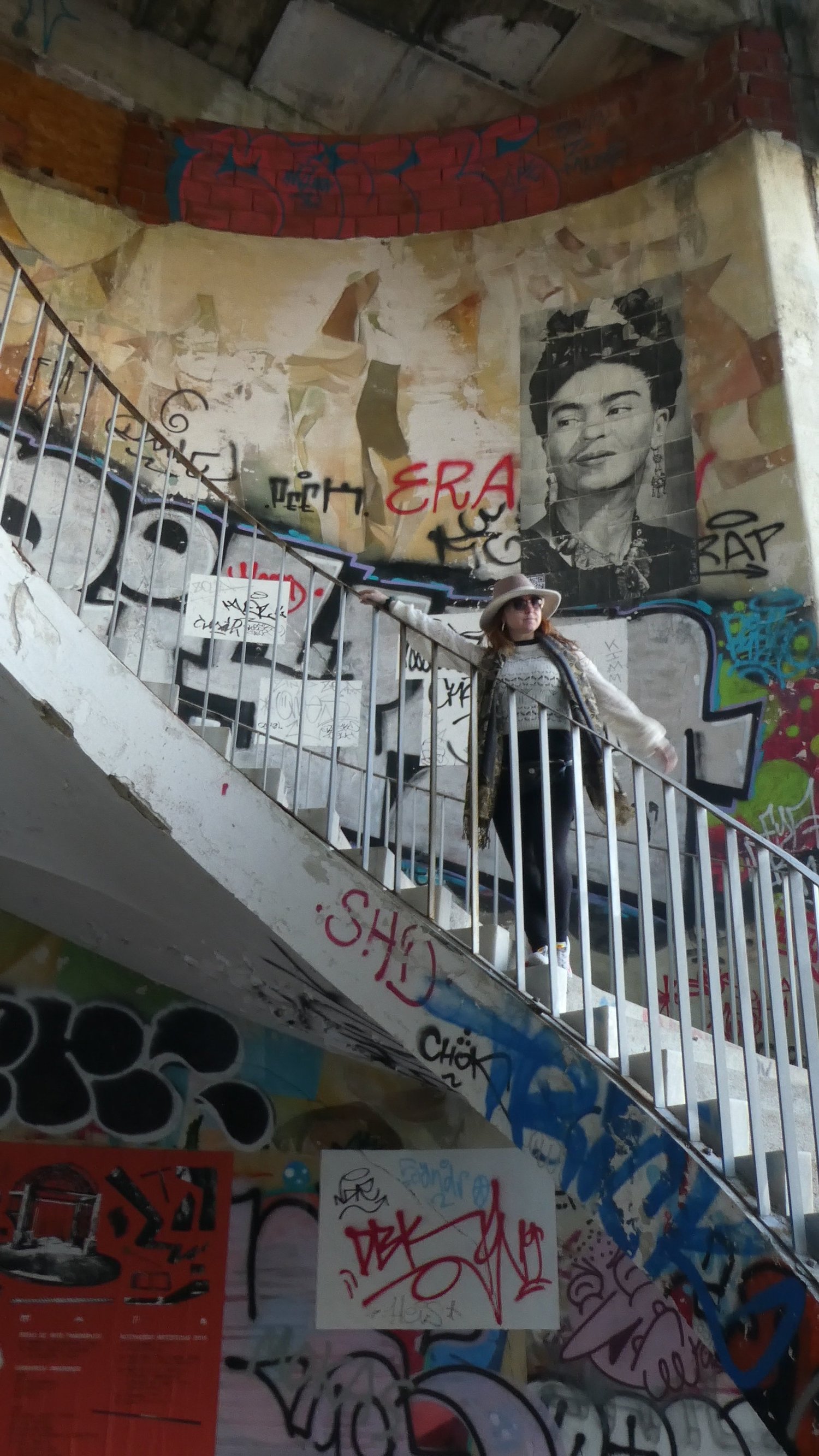 A visitor on the spiral staircase in front of a large mural portrait of Frida Kahlo