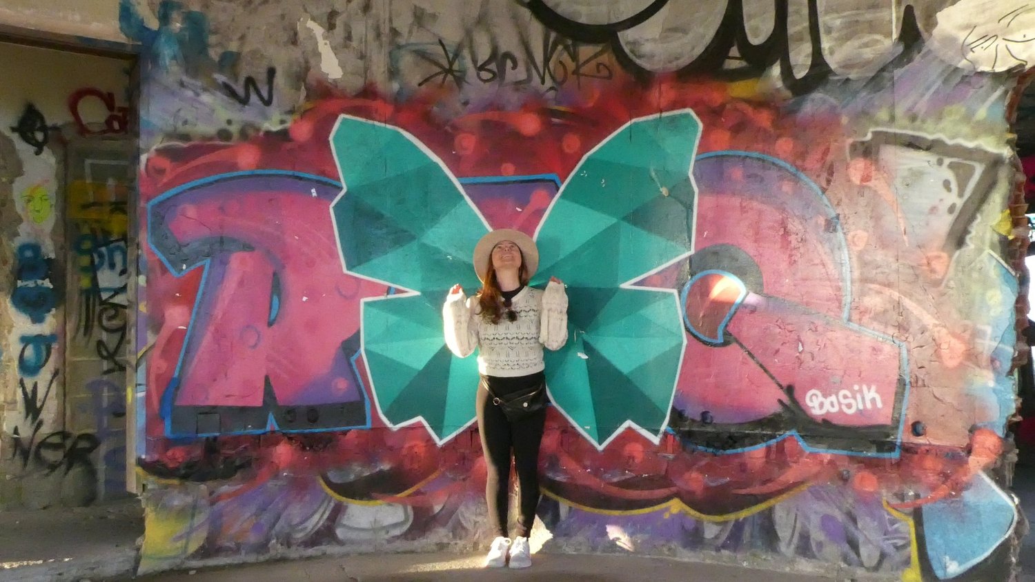 A visitor standing in front of a large pink and teal butterfly painted across the concrete wall