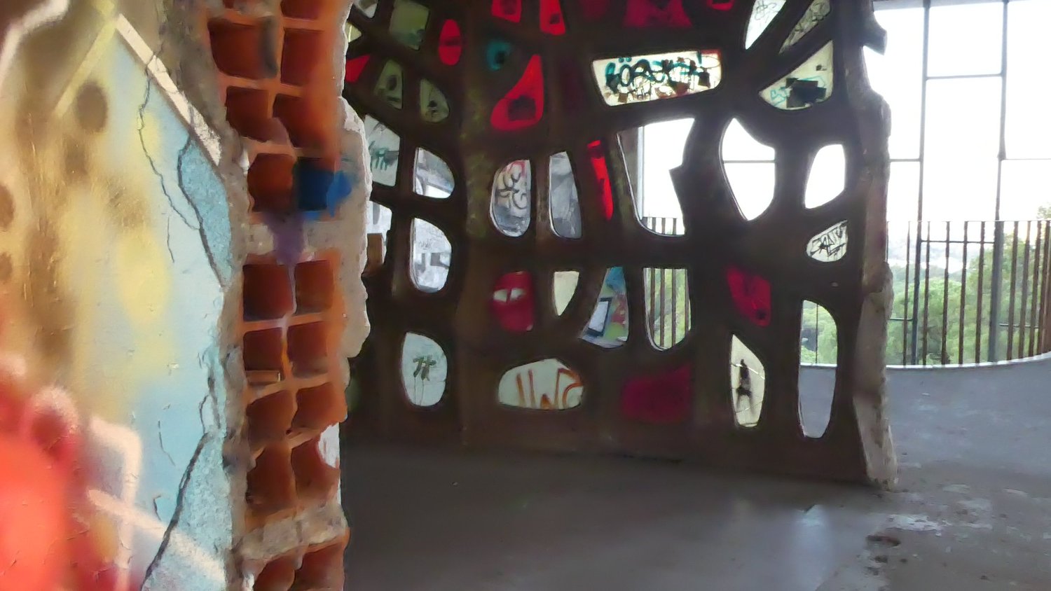 A sculpted concrete screen wall with organic shaped openings, painted red and looking out over the treetops