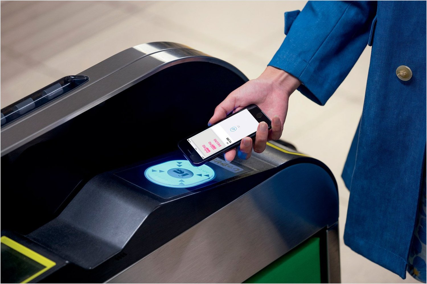 A hand holding an iPhone with a Pasmo card in Apple Wallet, tapping it against a Japanese ticket gate reader