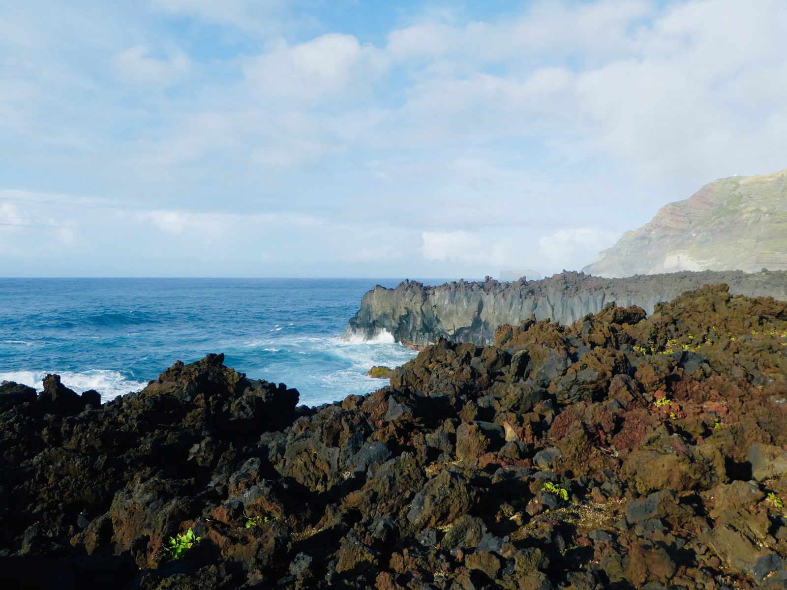 Black lava rock and turquoise water at the cove at Ponta da Ferraria, with the cliff rising behind