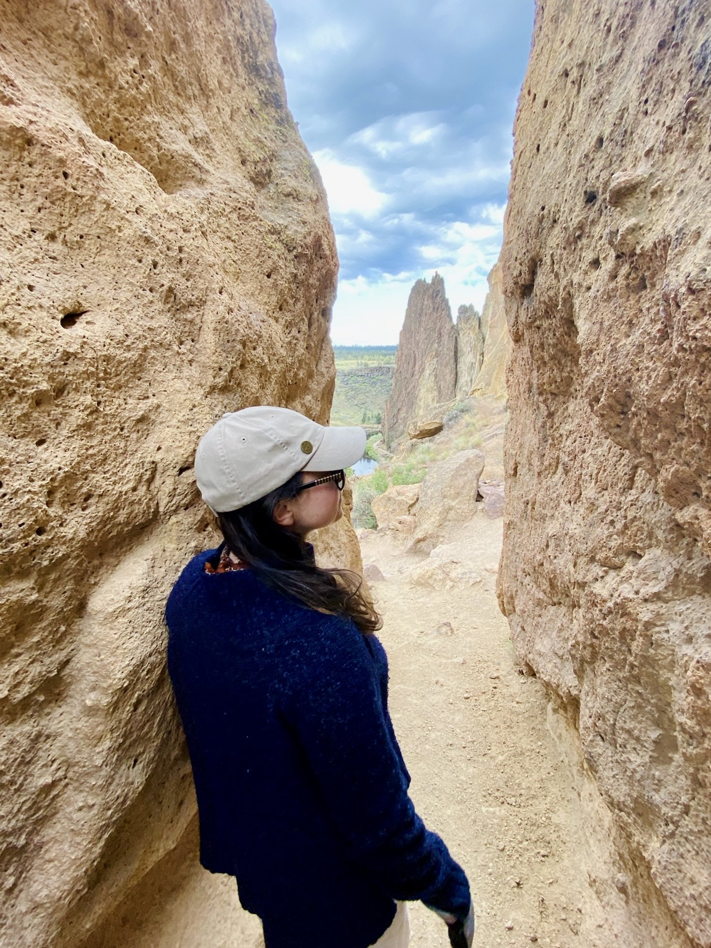 A hiker in a cap pausing in a narrow gap between two tall walls of tuff rock at Smith Rock