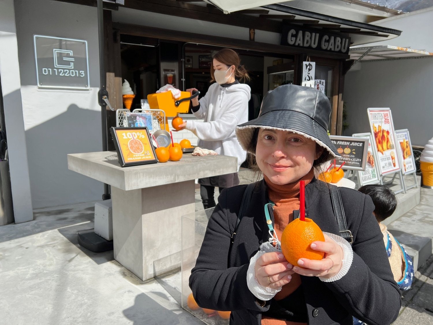 Holding a whole orange pressed into fresh juice with a straw at a street stand in Yufuin, Kyushu