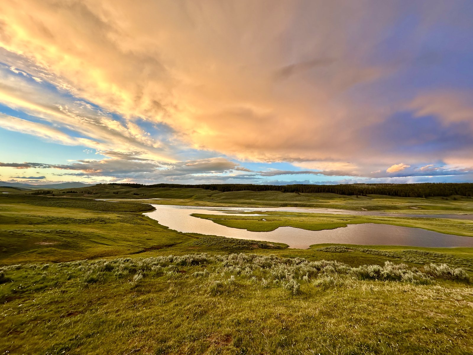 The Yellowstone River winding through Hayden Valley under an orange evening sky